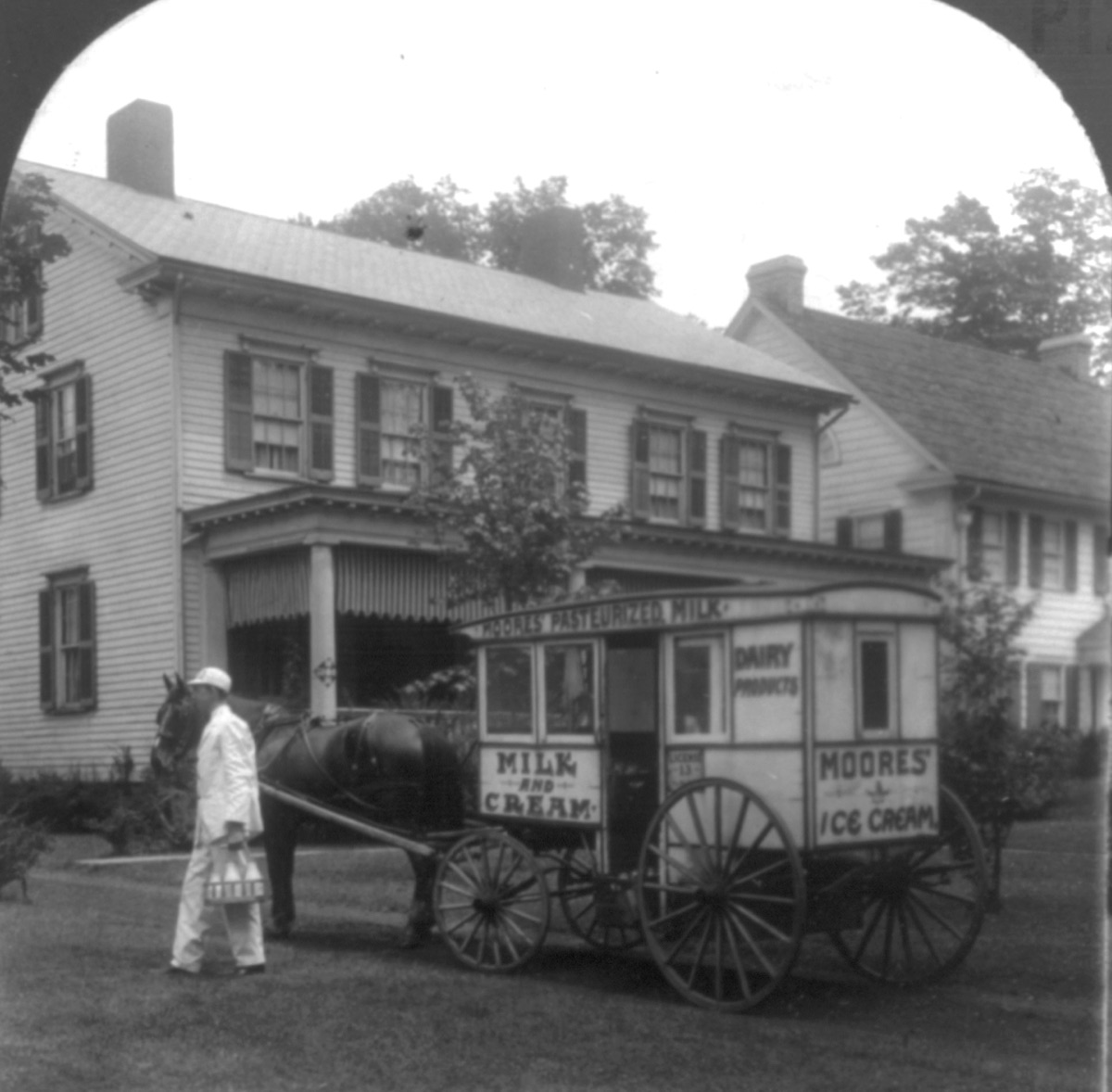A U.S. milkman with a delivery wagon, 1925, standing beside the cart loaded with glass bottles for residential doorstep delivery